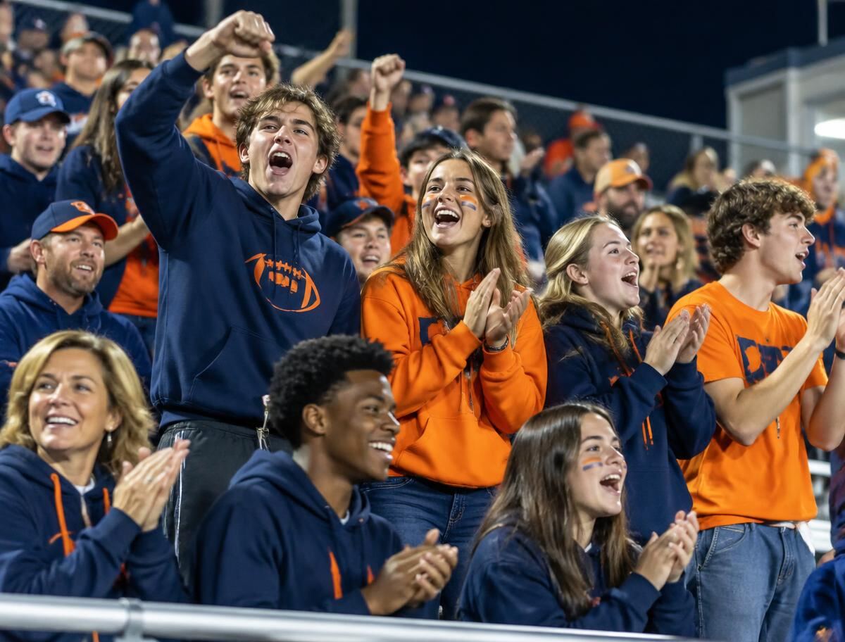 High school fans cheering in the stands wearing coordinated school spirit wear
